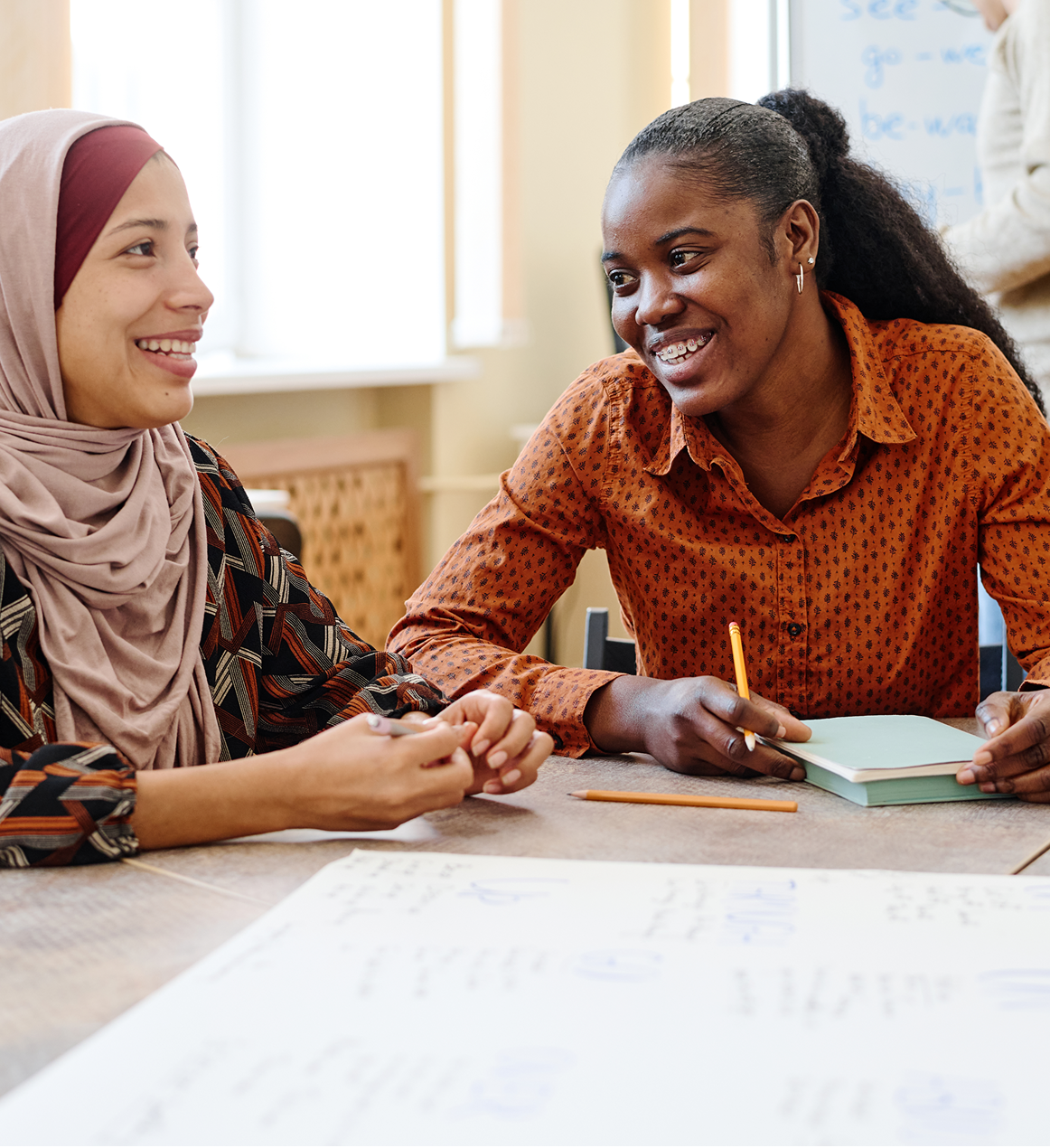 Two women smiling and discussing at table.